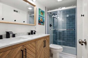 A modern bathroom with a wooden vanity, a white toilet, and a glass-enclosed shower. - Wave Watcher's Condo - Steps to the beach! (Ocean City)