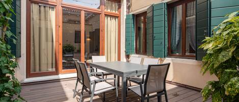 Eine Terrasse mit Tisch und Stühlen, eine Schiebetür und ein Fenster mit Fensterläden.