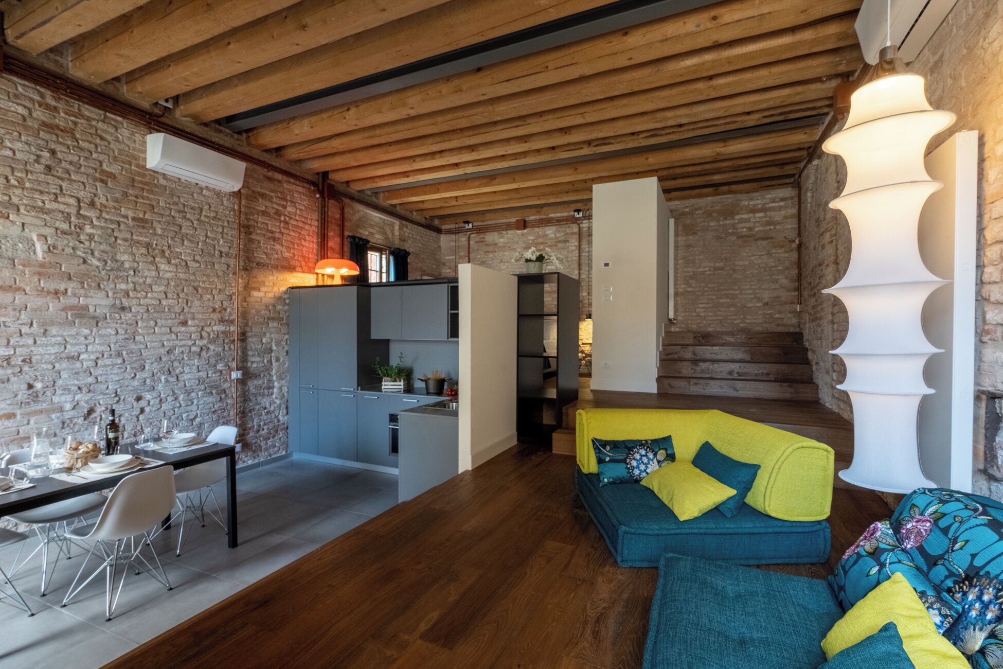 Una sala moderna con techo de madera, pared de ladrillo y un sofá con cojines coloridos.