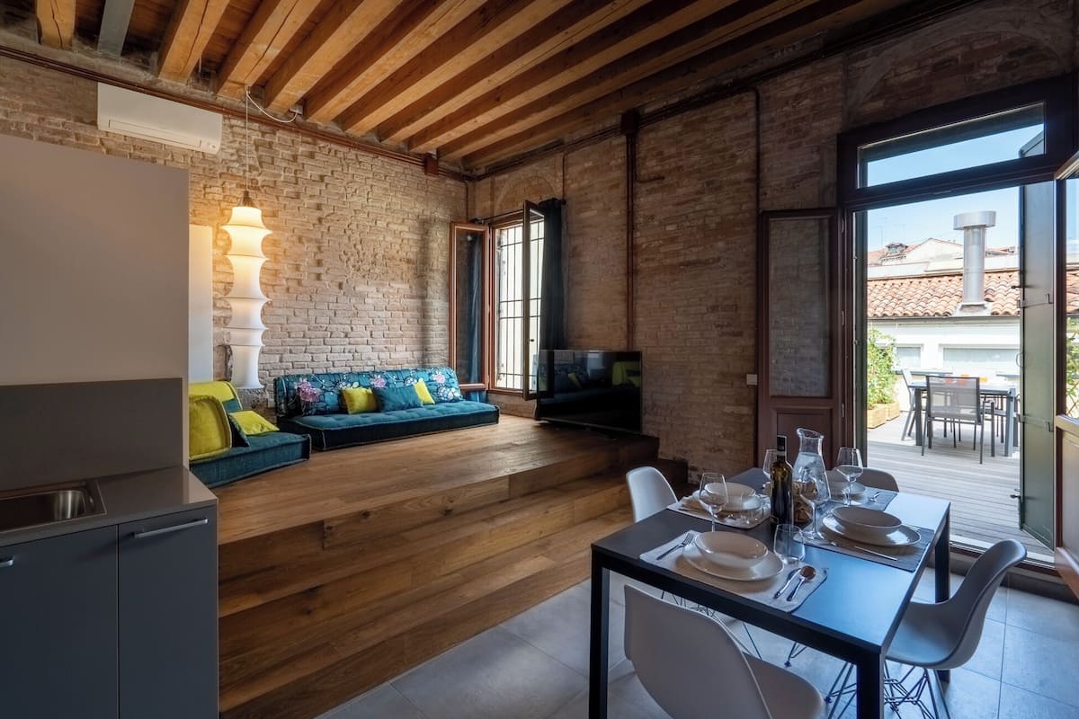 A modern kitchen with a built-in oven, a dining area with a table set for two, and a cozy seating area with a sofa and a TV.