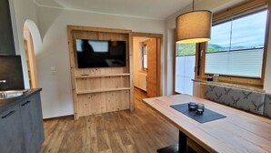 Una cocina moderna con un mueble de televisión de madera, una mesa de comedor con un mantel individual negro y una ventana con persianas.