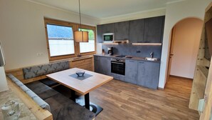 Una cocina compacta con horno integrado, microondas y lavabo. Hay un banco de madera con cojín y una mesa con un tazón.