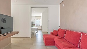 Un salon moderne avec un canapé rouge, un téléviseur posé sur un meuble en bois, et un coin repas à l’arrière-plan.