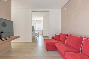 Una sala de estar moderna con un sofá rojo, un televisor sobre un mueble de madera y un comedor al fondo.
