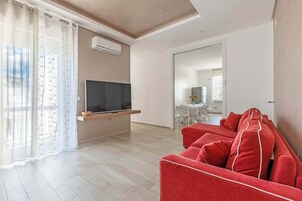 Una sala de estar moderna con un televisor de pantalla plana, un sofá rojo y un comedor al fondo.