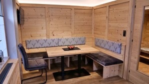 Een houten cabin met een zithoek met een bank, een tafel en een aan de muur bevestigde televisie.
