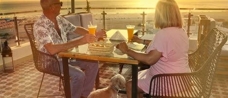 Un couple est assis à une table, profitant de la vue sur le coucher de soleil sur l’océan.