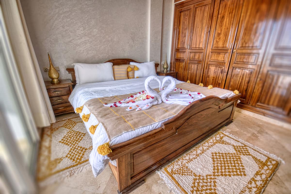 A neatly made bed with a patterned bedspread, a wooden headboard, and a wooden nightstand with a lamp.