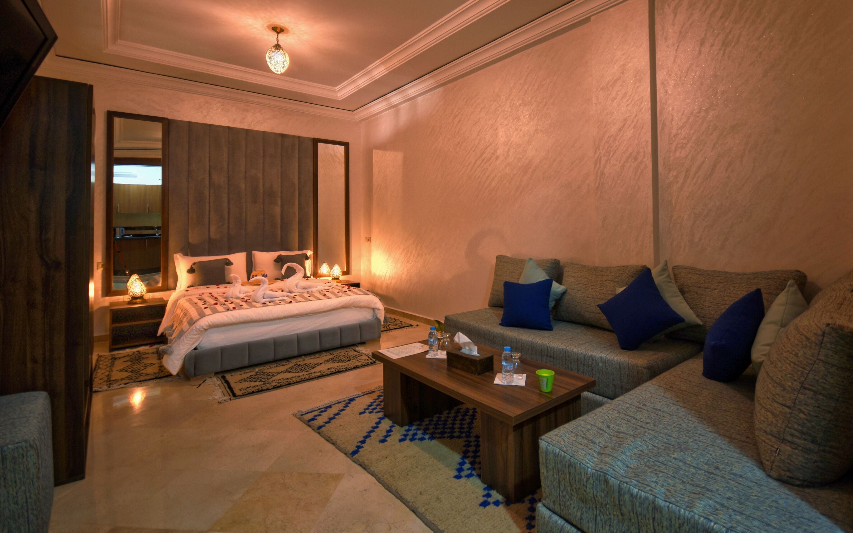 A modern hotel room with a large bed, a sofa, a coffee table, and a mirror.