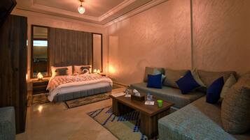 A modern hotel room with a large bed, a sofa, a coffee table, and a mirror.