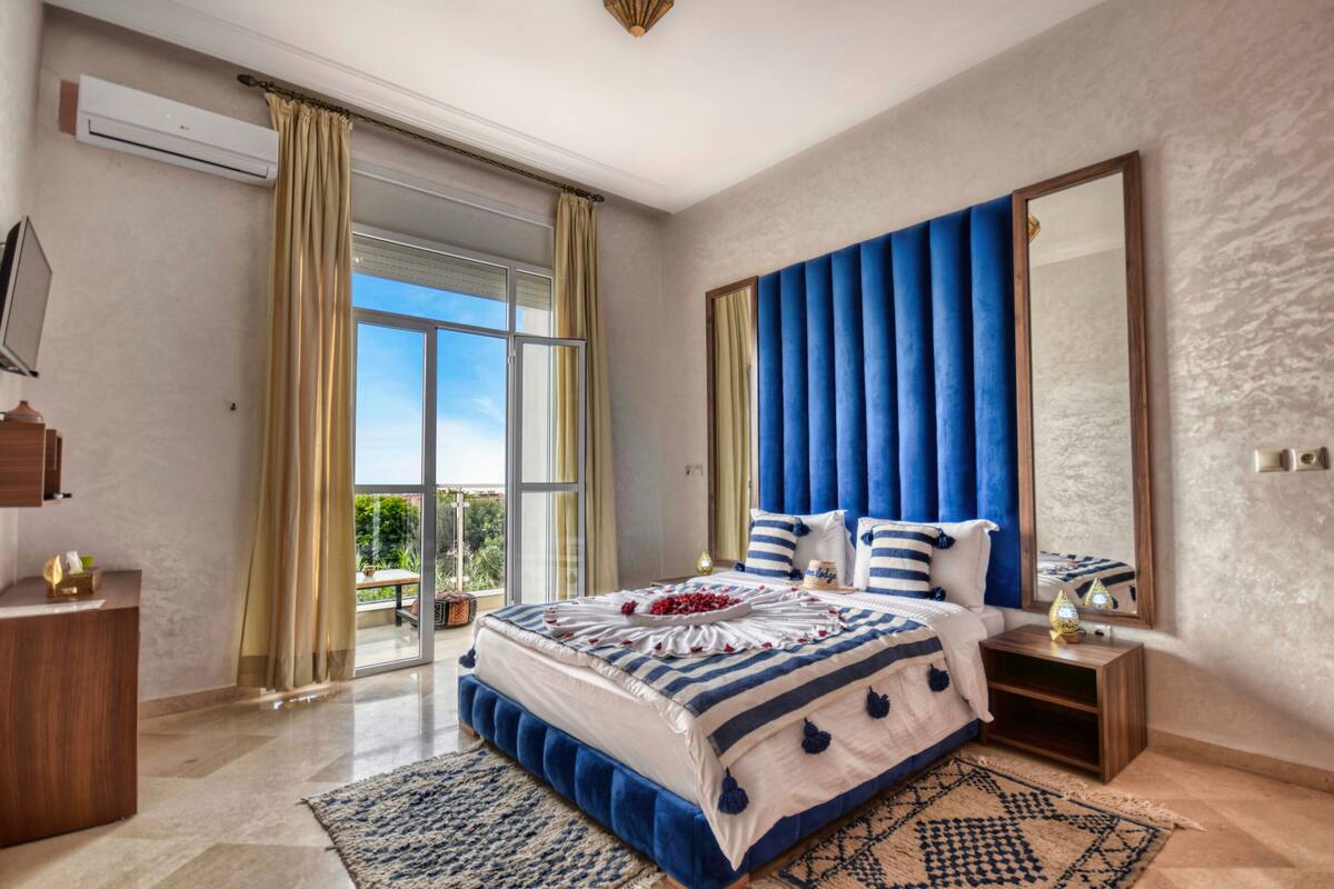 A bedroom with a large bed, a nightstand, a mirror, and a window with curtains.