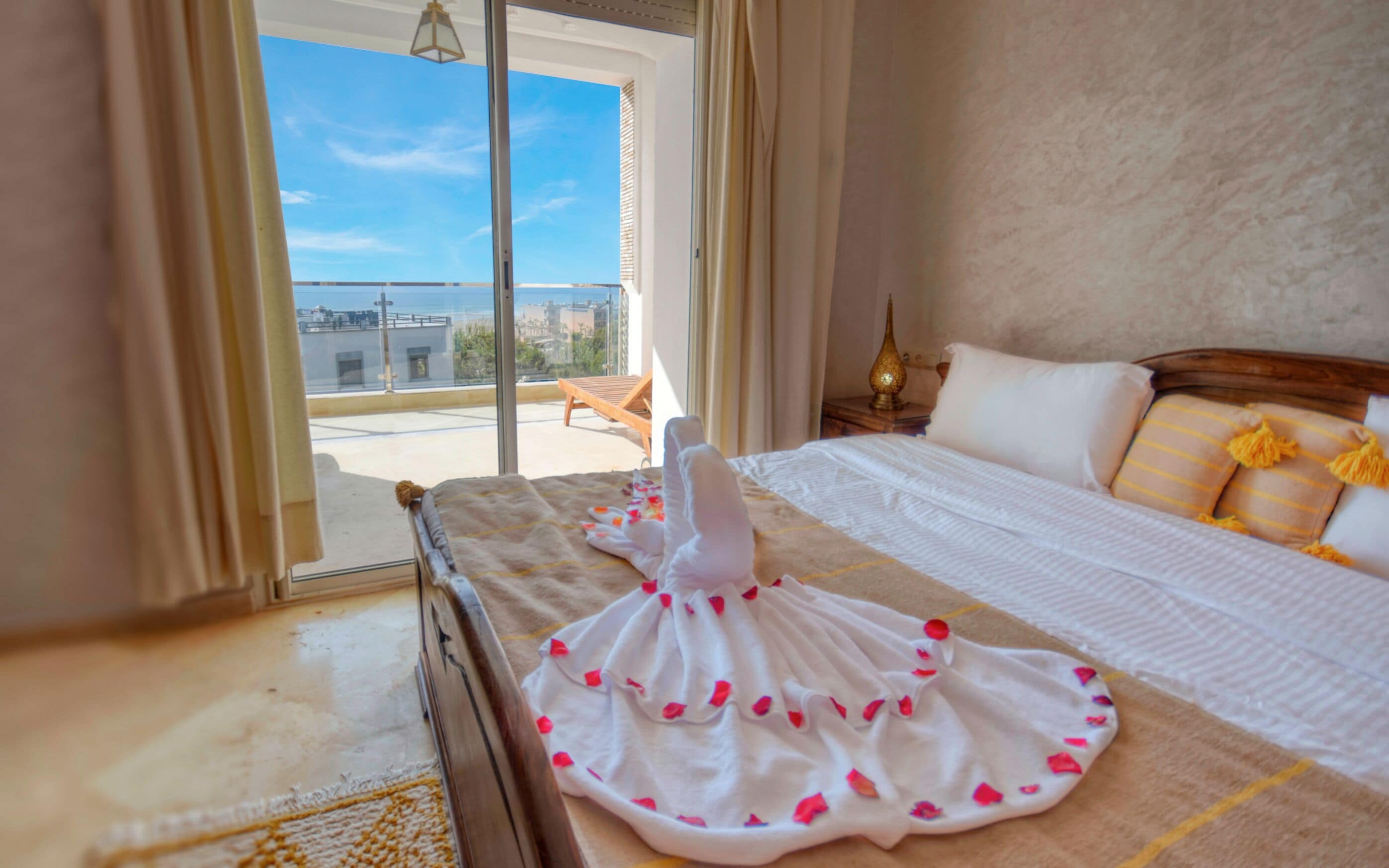 Habitación de hotel con cama, mesita de noche y vistas de la ciudad a través de un ventanal grande.