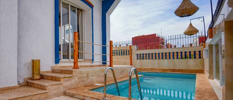 A rooftop pool with a clear view of the city skyline, a blue and white building with a large window, and a metal railing.