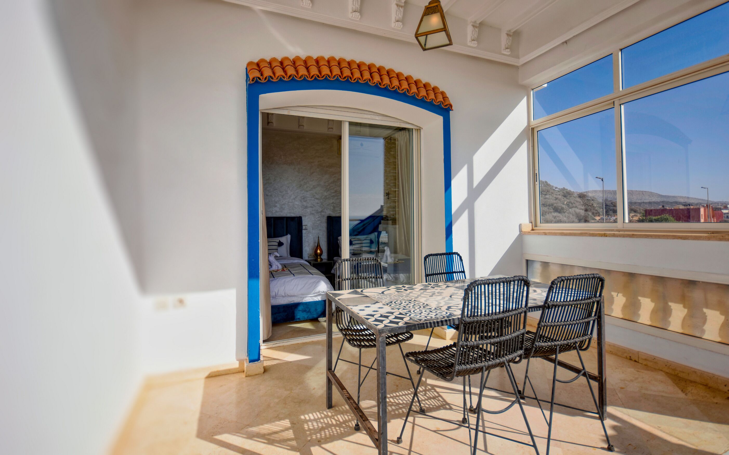 Un balcón con mesa y sillas, vista al exterior y una puerta que da a una habitación.