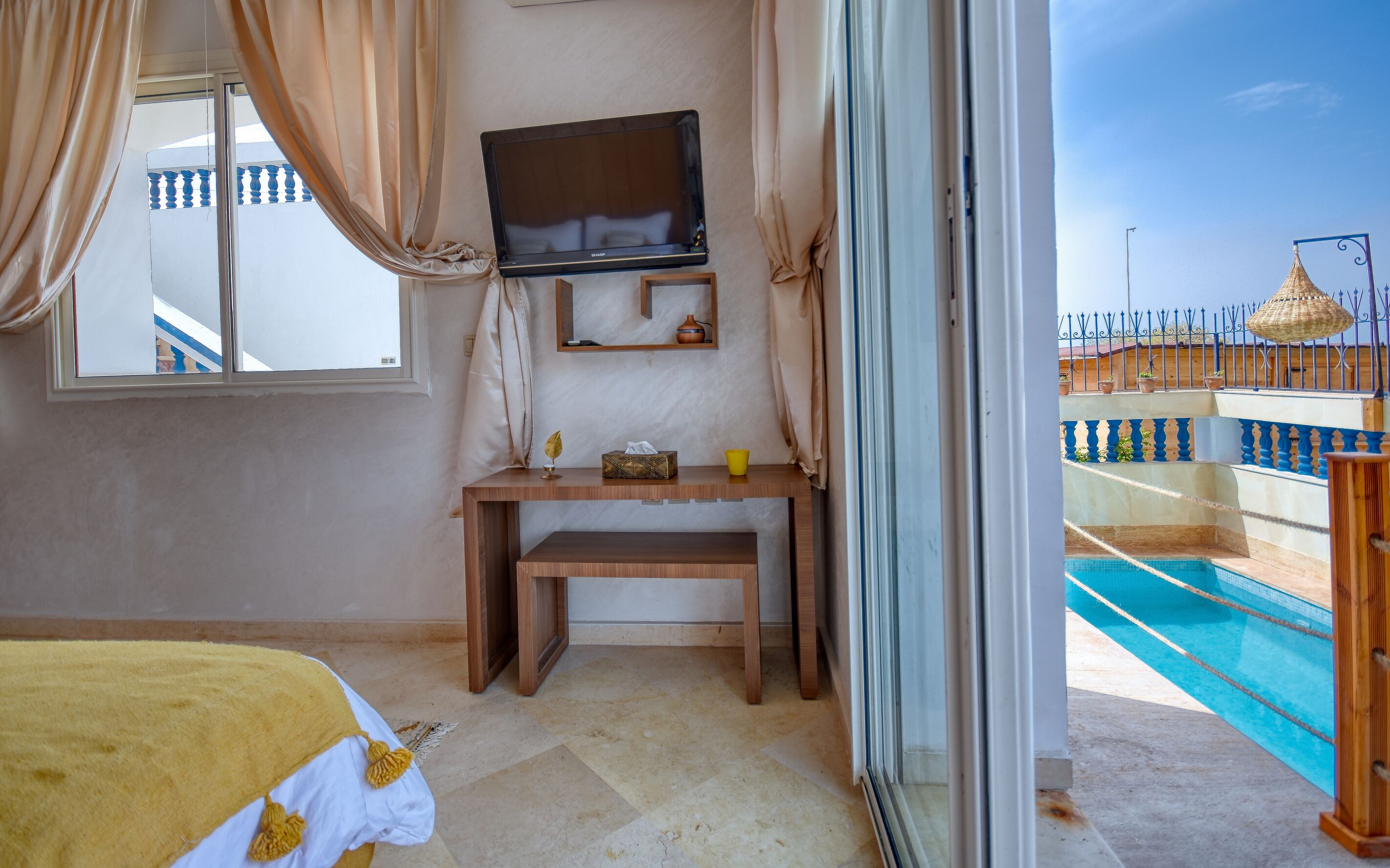 A room with a bed, a desk, a television, and a view of a swimming pool.