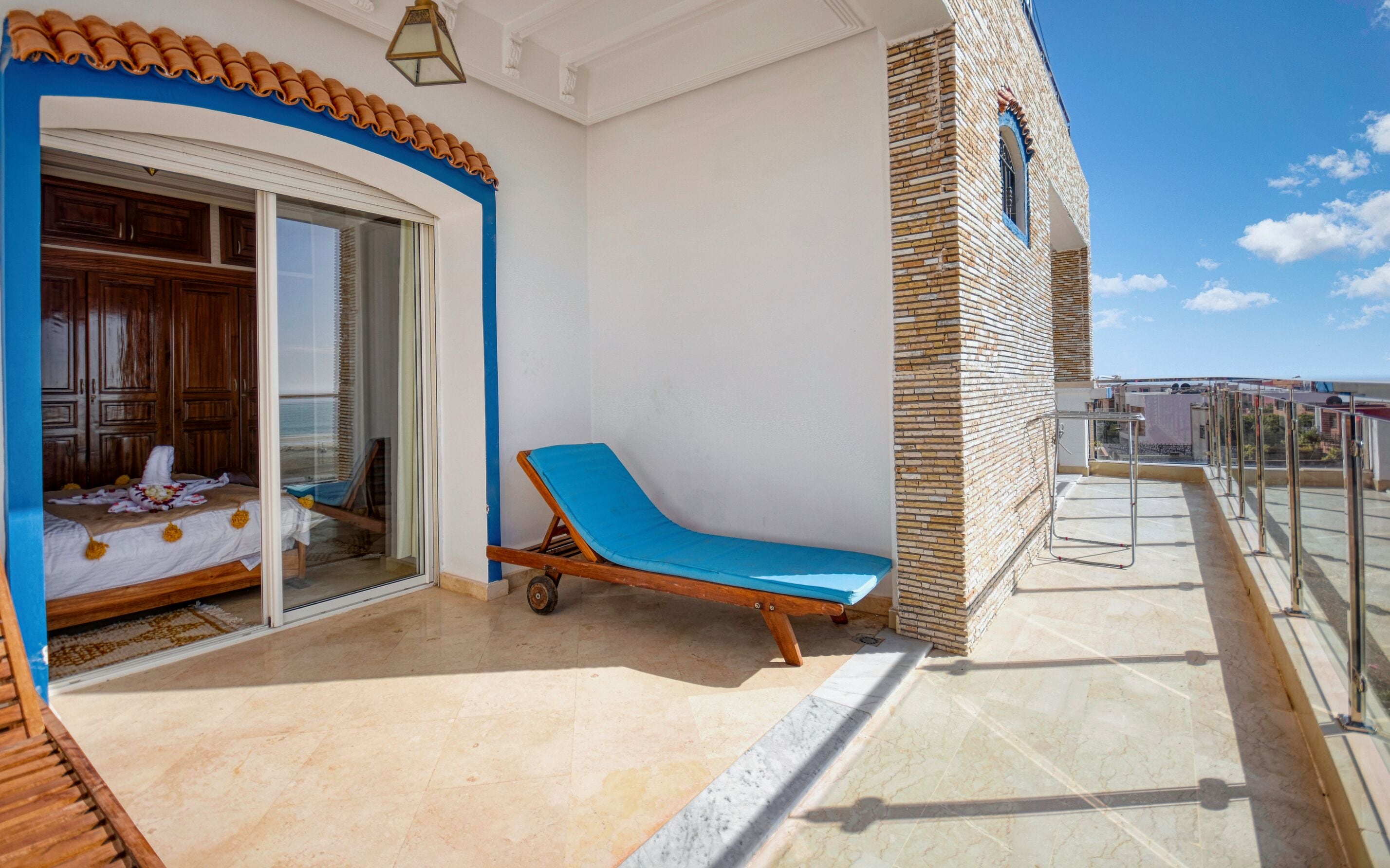 A balcony with a blue sun lounger, a wooden door, and a view of the city.