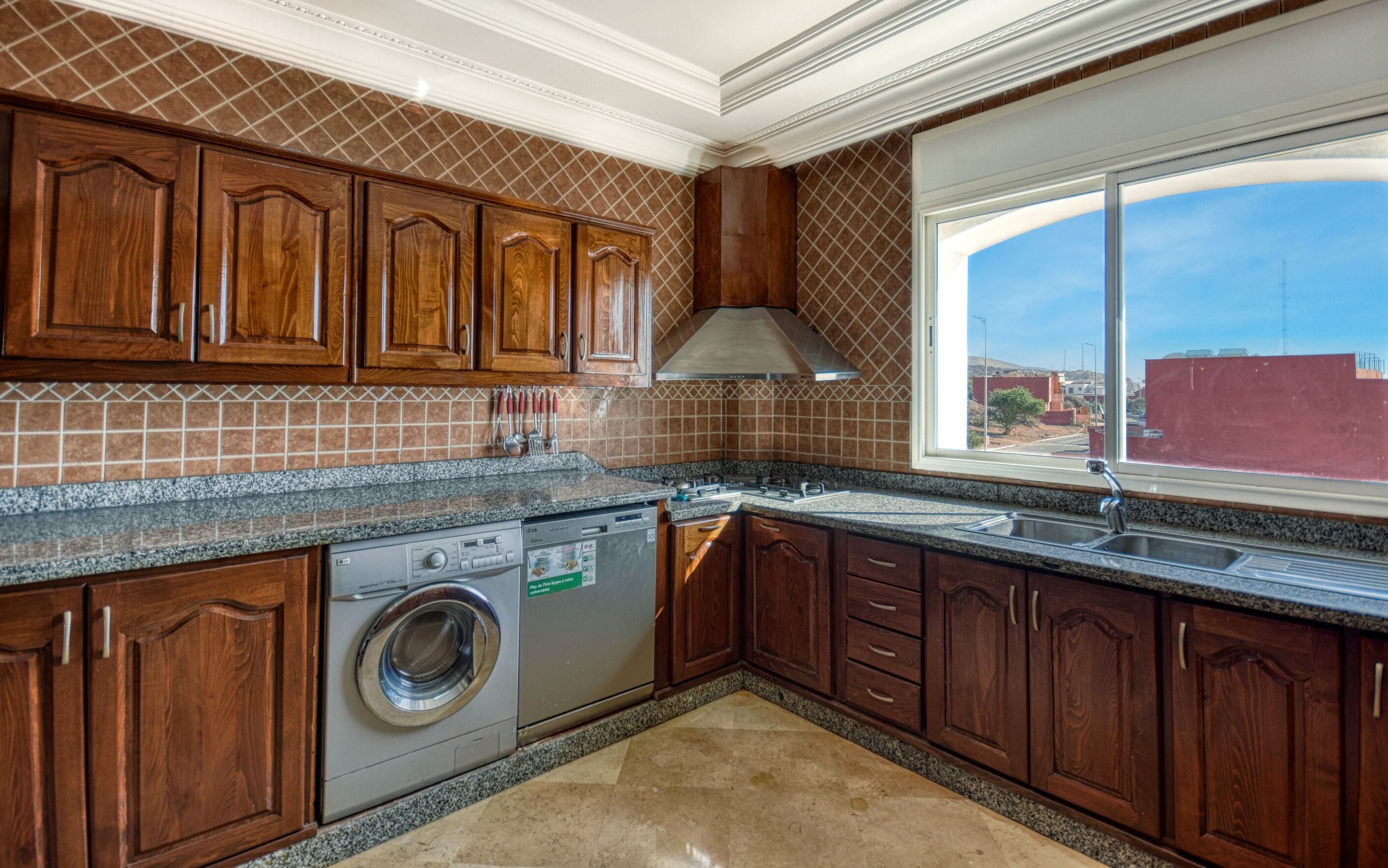A kitchen with wooden cabinets, a built-in dishwasher, and a window with a view of the outside.