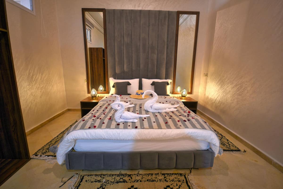 A neatly made bed with a striped bedspread, two bedside tables with lamps, and a large mirror above the bed.