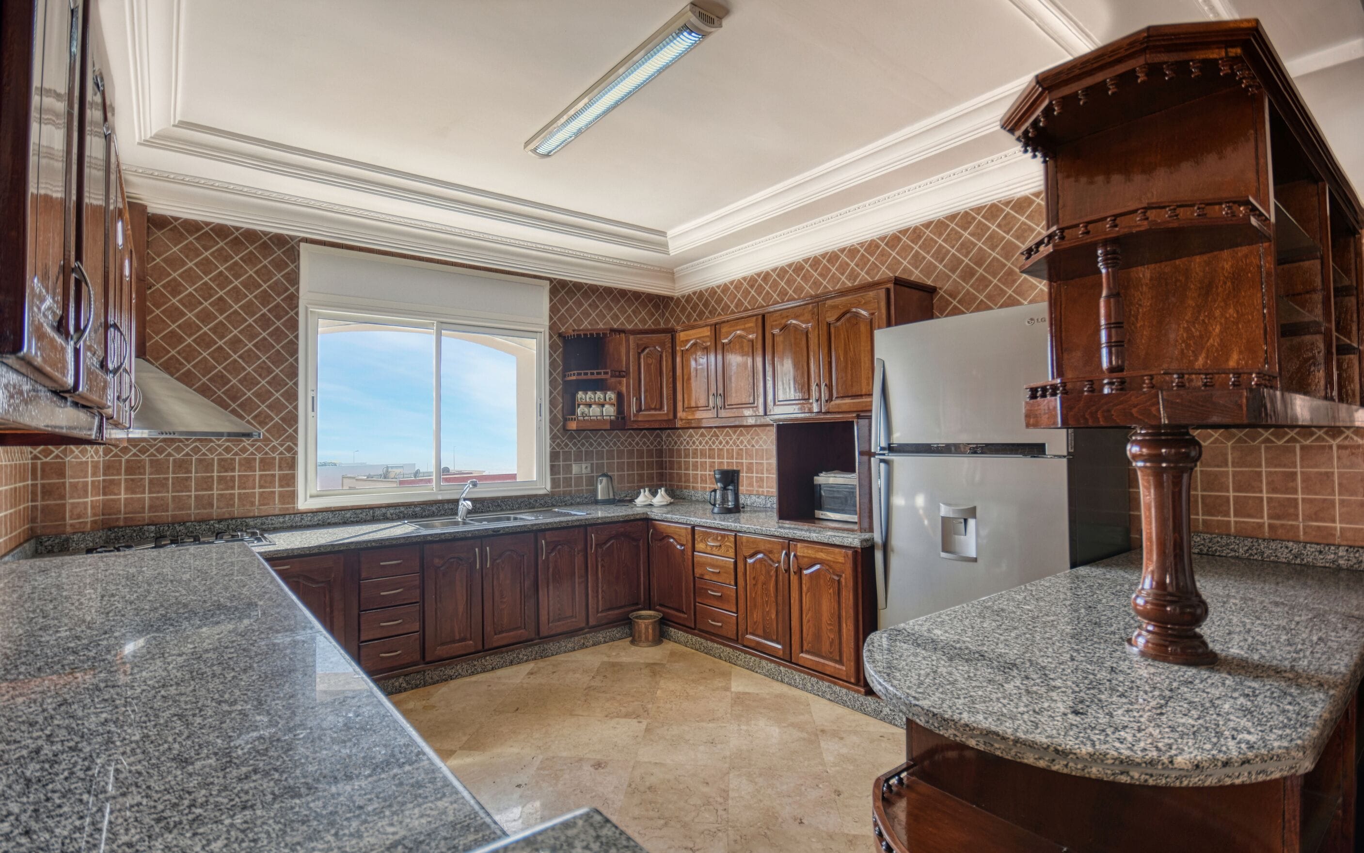 Una cocina con encimeras de granito, armarios de madera, un refrigerador de acero inoxidable y una ventana con vistas.