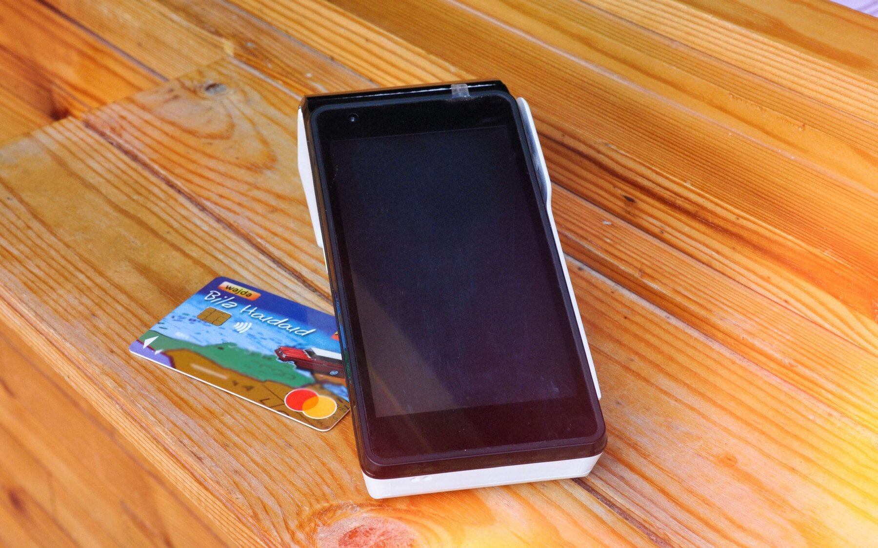 Un téléphone intelligent posé sur une surface en bois, avec une carte de crédit à côté.