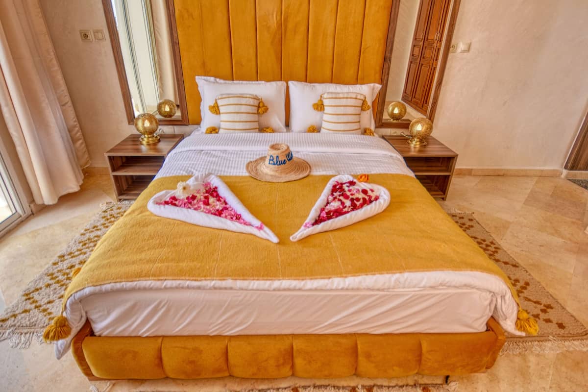A neatly made bed with a yellow headboard, white pillows, and a decorative heart-shaped towel arrangement.
