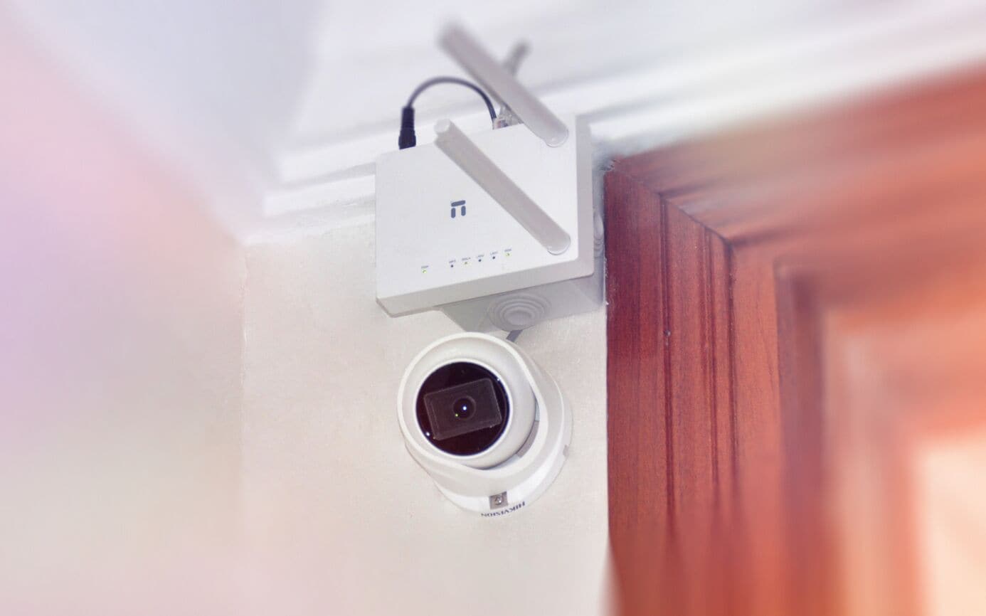 A white security camera mounted on a wall with a visible power outlet.