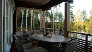 A covered outdoor seating area with wicker furniture and a table set for dining, overlooking a forested area.