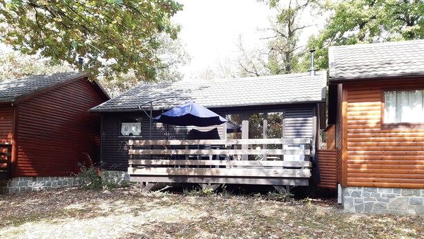 A cabin with a wooden deck, a blue umbrella, and a stone foundation.