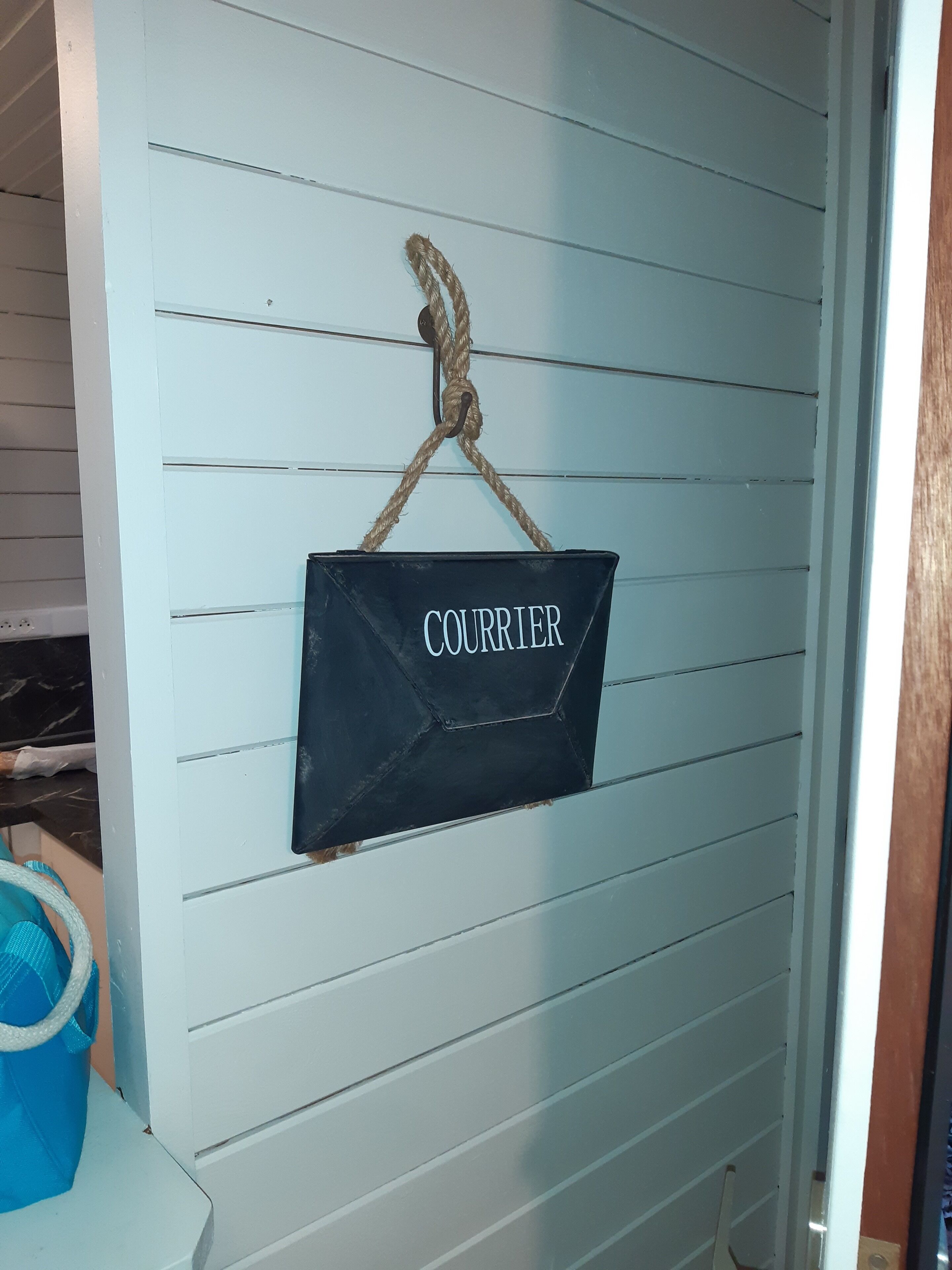 A sign with the word "COURRER" hanging on a light blue wall.