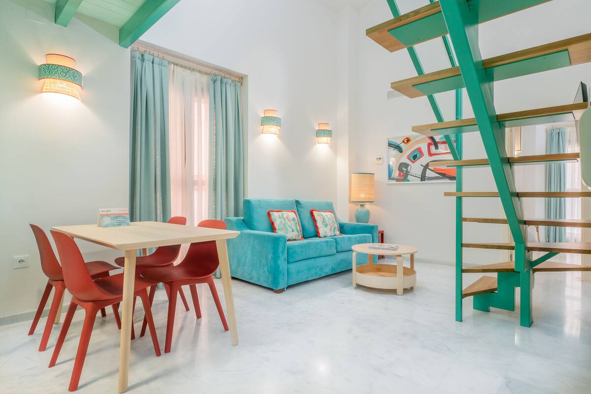 A modern living room with a blue sofa, red chairs, a wooden table, and a green staircase.