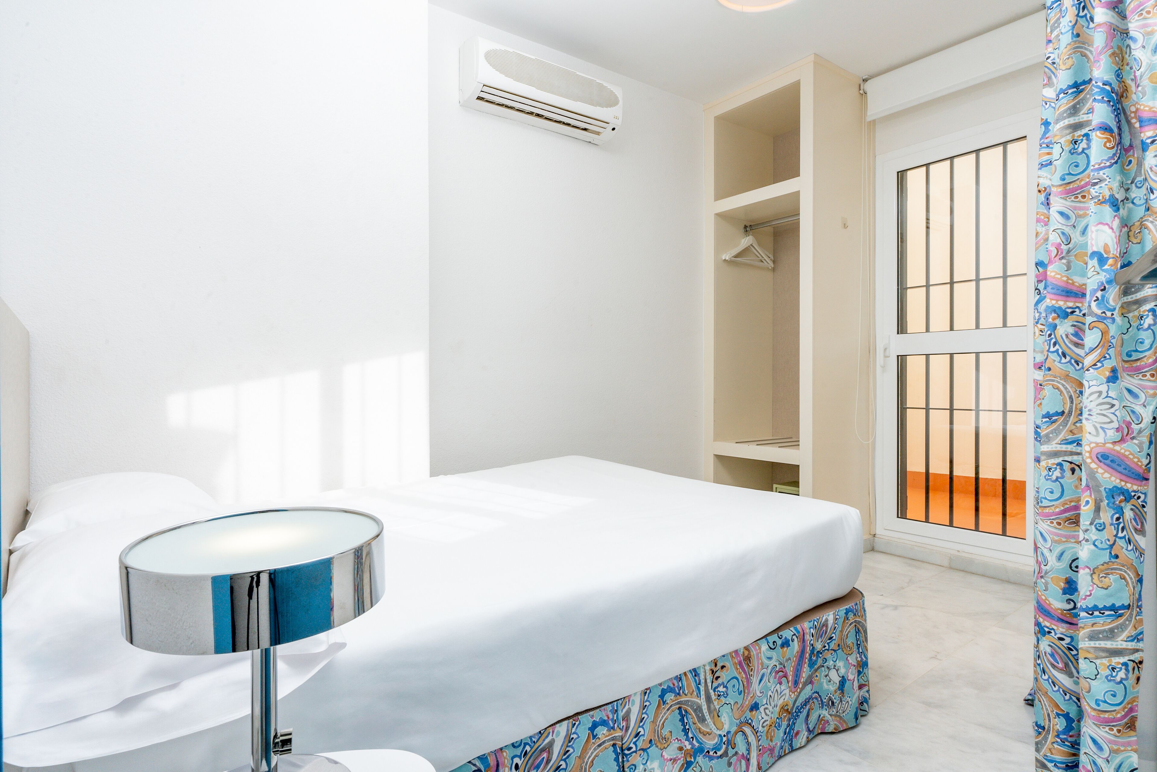 Un dormitorio con cama, mesita de noche, aire acondicionado, armario y ventana con vistas.