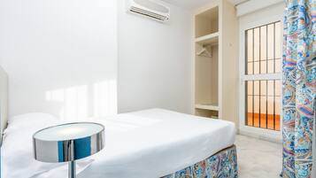 Un dormitorio con cama, mesita de noche, aire acondicionado, armario y ventana con vistas.