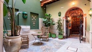 A courtyard with a wicker chair, a table, potted plants, and a large vase. - Smartr Sevilla Las Dueñas (Seville)