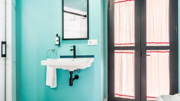 Un bany amb una paret color turquesa, un lavabo blanc, un mirall i una porta amb cortines vermelles.