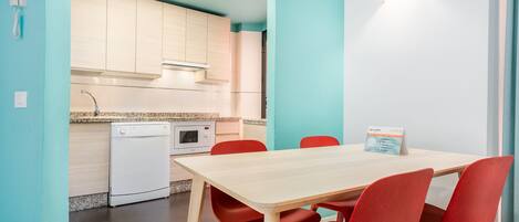 A compact kitchen with a dishwasher, microwave, and a small oven. There is a table with four red chairs and a light fixture on the wall.