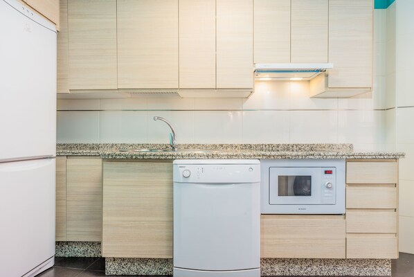 Cocina compacta con lavadora y secadora integradas, microondas y encimera de granito.