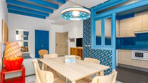 A modern kitchen with blue accents, a dining area with a wooden table and chairs, and a red chair with a patterned cushion. - Smartr Sevilla Las Dueñas (Seville)