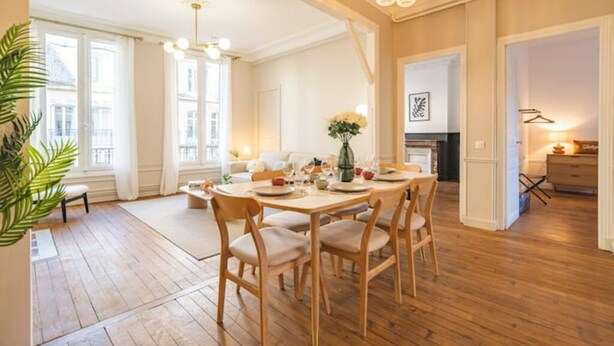 A dining area with a wooden table and chairs, a vase with flowers, and a hanging light fixture. - Le Champagne Central (Reims)