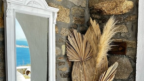 A stone wall with a white-framed mirror and a small white table with a vase of dried plants. - Vougli View (Mykonos)