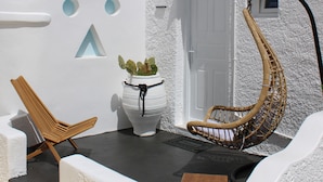 A white building with a door, a potted plant, a wicker chair, and a wooden stool. - Vougli View (Mykonos)