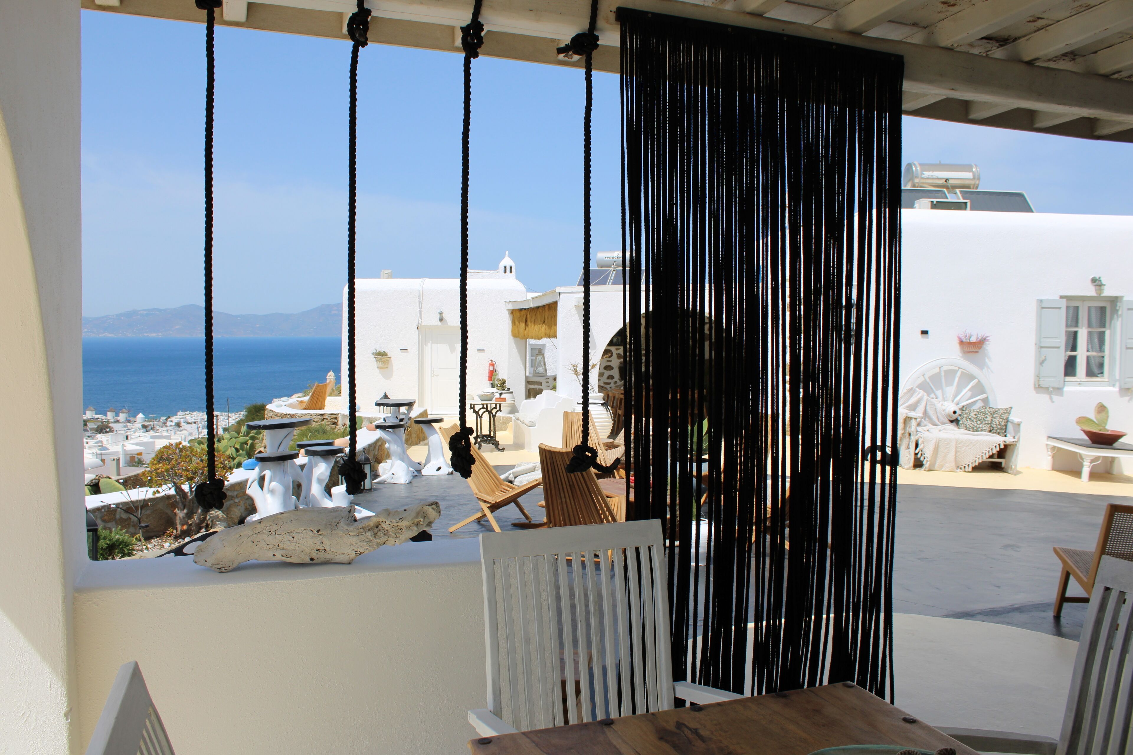 A terrace with a view of the sea, white buildings, and a wooden table.