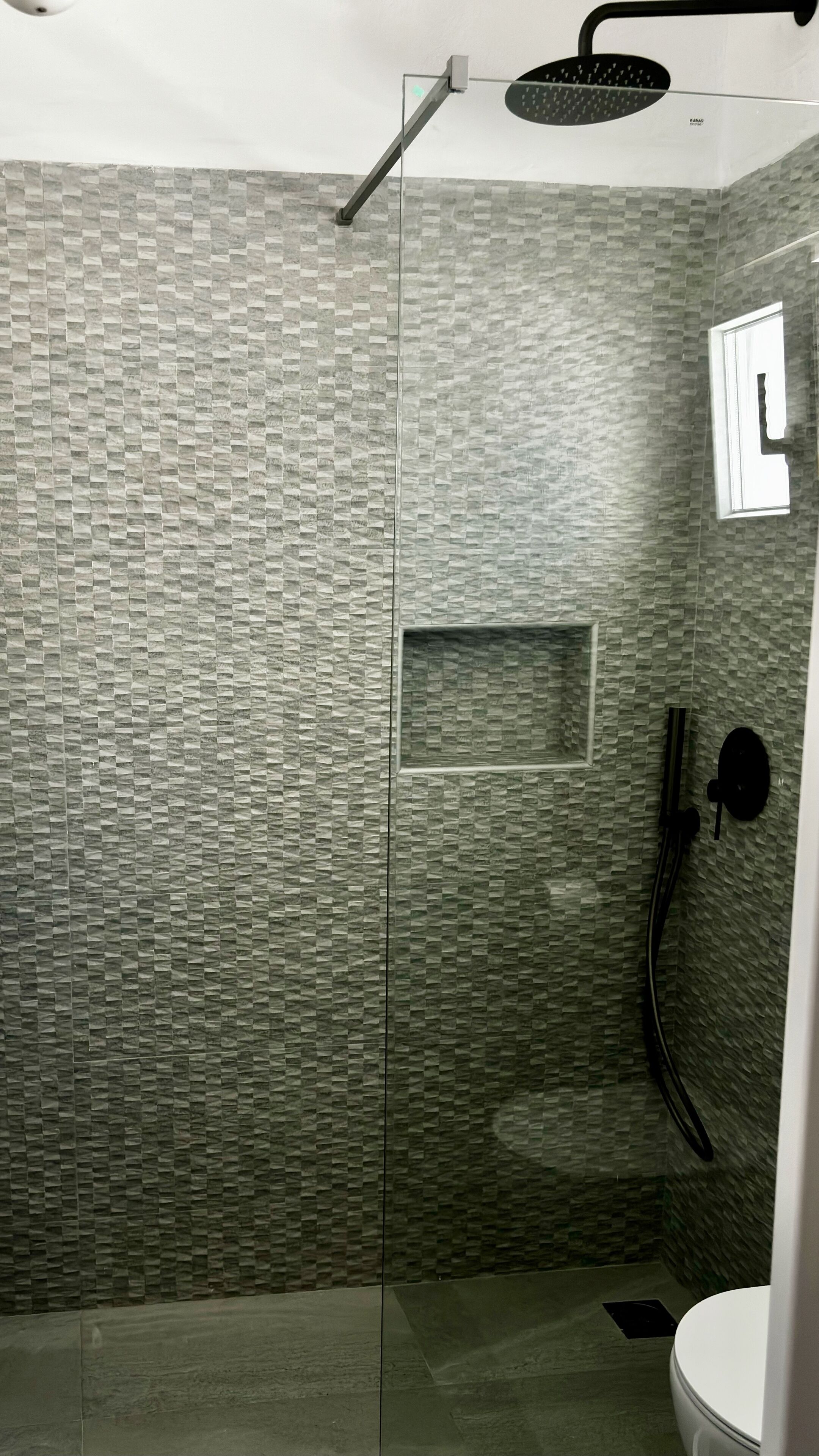 A modern shower area with a textured wall, a glass door, and a handheld showerhead.