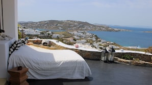 A bedroom with a bed, a small wooden stool, and a view of a coastal town and sea. - Vougli View (Mykonos)