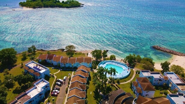 Vista aérea de un complejo turístico con piscina, acceso a la playa y varias edificaciones.