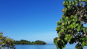 Paisaje costero con agua azul cristalina, costa rocosa y una isla distante.