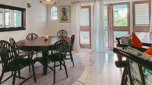 Un comedor con una mesa redonda y sillas, un sofá con cojines y ventanas grandes con cortinas.