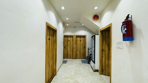 A hallway with wooden doors, a fire extinguisher, and a clock on the wall. - Hotel Shree Mahakal Krapa (Ujjain)