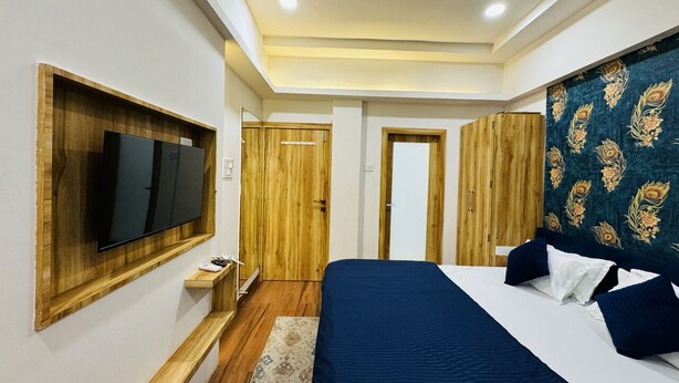 A bedroom with a large bed, a TV mounted on a wooden shelf, and a wardrobe with a peacock pattern. - Hotel Shree Mahakal Krapa (Ujjain)