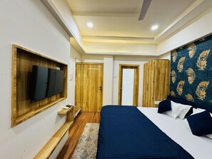 A bedroom with a large bed, a TV mounted on a wooden shelf, and a wardrobe with a peacock pattern. - Hotel Shree Mahakal Krapa (Ujjain)