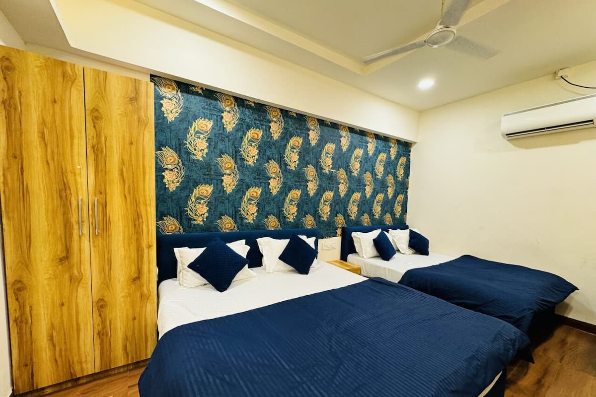 Quarto com duas camas, guarda-roupa de madeira, ventoinha de teto e aparelho de ar condicionado.